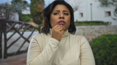 Düşünceli bir yüz ifadesi olan bir kadın, şehir çevresi ve doğal yeşillik zeminine karşı tuhaf bir tavır sergiliyor..