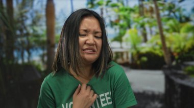 Yeşil gönüllü gömlekli bir kadın açık hava parkında, yemyeşil ortamda otantik duyguları yakalama konusunda tiksinti gösteriyor. Anahtar sözcükler arasında kadın, gönüllü, yeşil, tiksinti, açık hava.