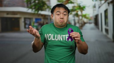 Gönüllü gömleği giyen genç bir adam, şehir sokaklarında mor bir kurdele tutuyor, hareketli bir şehirde farkındalık çabalarını simgeliyor..