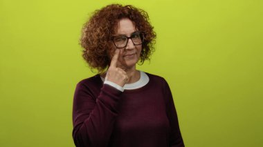 Gözlerini gösteren gözlüklü orta yaşlı bir kadın. Parlak sarı bir arka planda izole edilmiş..