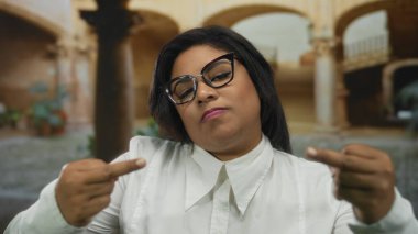 Eski bir üniversite avlusunda genç bir kadın açık hava ortamında küstah bir ifade sergiliyor, kültürel mirasın ve modern tutumun özünü yakalıyor..