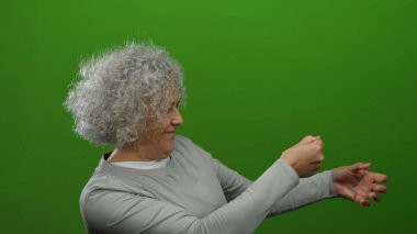 Gri saçlı yaşlı kadın, yeşil arka planda ip çekiyor, hareket ve kararlılık gösteriyor..