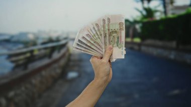 Açık bir sokak ortamında Rus rublesi banknotları tutan, döviz kurunu veya ekonomik konsepti finansal unsurlar ve kentsel çevre üzerine odaklı gösteren bir adam.
