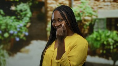 Şehir merkezinde açık havada gülümseyen parlak sarı gömlekli, yemyeşil arka planlı bir kadın güneşli bir günde günlük yaşam tarzını ve hareketli bir havayı simgeliyor..