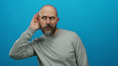 Mavi arka plan karşısında dikkatle dinleyen bir adam stüdyoda izole edilmiş ve hakiki duyguları yakalayan tuhaf bir ifade yaratır.