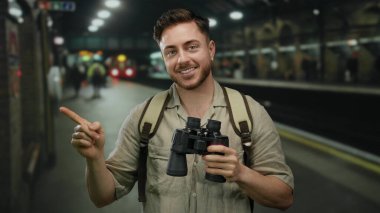 Dürbünlü sakallı genç bir adam ve hareketli bir tren istasyonunu işaret ederek seyahat ve keşif ruhunu gösteriyor..