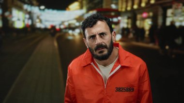 Hapishane tulumu giyen İspanyol sakallı adam gecenin bir yarısı kalabalık bir şehir sokağında bulanık ışıklarla dikiliyor..