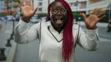 Şehir caddesinde pembe örgülü bir kadın duygularını dışa vuruyor, canlı saçlar, modern şehir geçmişi, gözlük takıyor ve hayat dolu kentsel yaşam tarzı izlenimi veriyor..