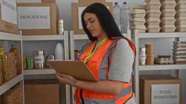 Bağış toplayan bir kadın, gıda malzemelerinin arasında gönüllü yelek giyiyor, organizasyonu ve toplum desteğini resmediyor..
