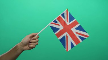 Yeşil arka planda İngiliz bayrağı tutan adam, açık bir şekilde milliyet ve renk karşıtlığını vurgulayan Birleşik Krallık kimliği sergiliyor..