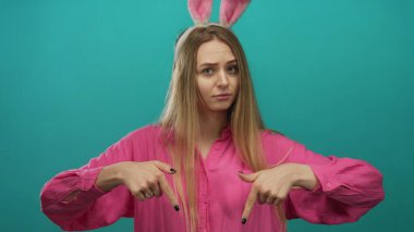 Pembe gömlekli ve paskalya tavşanı kulaklı bir kadın canlı yeşil bir arka plana doğru hareket ediyor. Yaratıcı ya da şenlikli kavramlar için izole edilmiş..