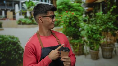 Gözlüklü ve önlüklü genç adam şehir sokaklarında elinde kahve fincanı tutarken yemyeşil bitkiler ve modern bir şehir geçmişi vardı..