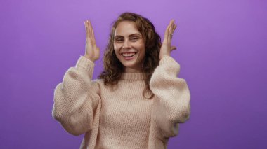 Rahat süveter içinde gülümseyen kadın, canlı mor arka plana karşı çerçeveleme hareketi yapıyor, yaratıcılık ve neşe ifade ediyor..