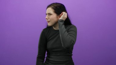 Esmer saçlı bir kadın, mor arkaplana karşı kulak misafiri oluyor. Merakını ve dikkatliliğini dile getiriyor.