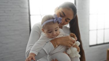 Sıcak bir oturma odasında bebeği tutan bir kadın, sıcak, sevgi dolu bir atmosferle, kapalı bir ortamda aile sevgisini ve şefkatini sergiliyor..