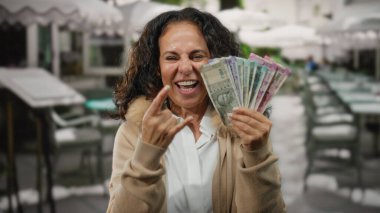 Orta yaşlı bir kadın Hindistan 'da bir restoranın terasında gülümsüyor ve elinde Hint rupisi banknotları tutarken parmaklarıyla taş gibi bir jest yapıyor..