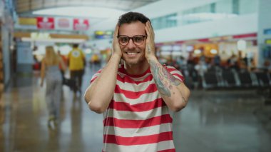 Yoğun bir havaalanı terminalinde sevinçten sırıtan çizgili tişörtlü genç adam, yolcularla çevrili seyahat planları ve canlı iç mekanlar hakkındaki heyecanını sergiliyor..