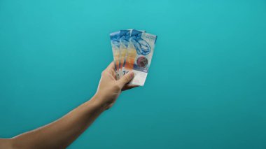 İsviçre banknotlarını izole edilmiş mavi arka plan duvarına dayayan adam, para yönetimi ve finans kavramını vurguluyor.