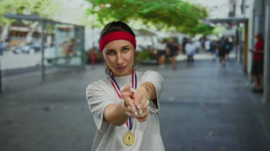 Madalyalı genç bir kadın şehir sokaklarında şen şakrak poz veriyor. Kırmızı saç bandı ve beyaz gömlek giyiyor..