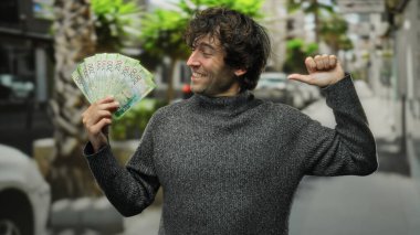 Şehirde elinde Rus rublesi tutan İspanyol bir adam, bir gülümseme ile kendine işaret ediyor, bir şehir sokak ortamında başarı ve zenginliği vurguluyor..