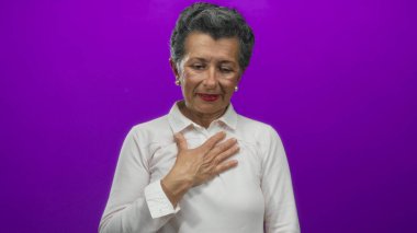 Beyaz tişörtlü, gri saçlı son sınıf öğrencisi bir kadın duygularını ifade ediyor. Göğsünde canlı mor bir arkaplan var. Gözleri yavaşça kapanıyor..