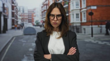 Gözlüklü kadın hareketli bir şehir sokağında kollarını kavuşturarak duruyor. Şehir yaşamında önemli bir anı yakalıyor. Kararlılığı ve odaklanmayı gösteriyor..