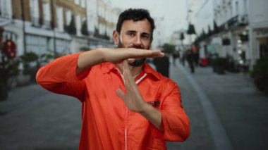 Turuncu tulumlu bir adam hareketli bir caddede dikilirken, çevresindeki şehir hayatı ile basitlik ve karmaşıklığın bir karışımını somutlaştırıyor..