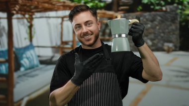 Sakallı, önlük takan genç bir adam, elinde kahve makinesiyle bir Fransız Kafe 'sinde garsonluk yapıyor..