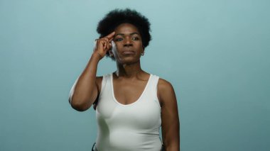 Beyazlı kadın alnına dokunuyor, parmağı mavi arka planda, izole edilmiş arka planda düşüncelerini aktarıyor..