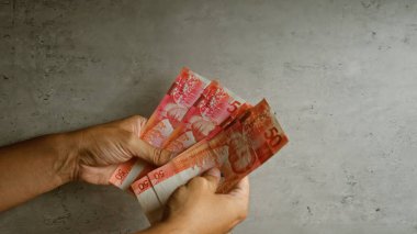 Elleri, arka planda birkaç Filipin pesosu tutuyor.