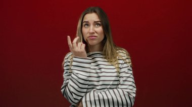 Katı kırmızı arka planda endişeli bir kadın, çizgili bir gömlek giyiyor, yalnız bir ortamda endişe ve düşüncelere dalmış..