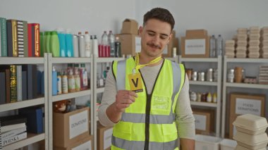 Yansıtıcı yelek giyen genç İspanyol, hayır kurumunda gönüllü olarak çalışıyor. Etrafı kutular ve malzemelerle çevrili. Organize ve destekleyici bir ortam..