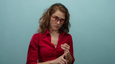 Kırmızı gözlüklü bir kadın mavi arka plan duvarına karşı parmaklarını sayarak düşünceli bir ifade sergiliyor..