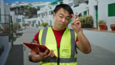 Şehir caddesinde duran genç adam elinde bir not panosu tutarken sarı bir güvenlik yeleği giyiyor ve düşünceli bir ifadeyle hareket ediyor..