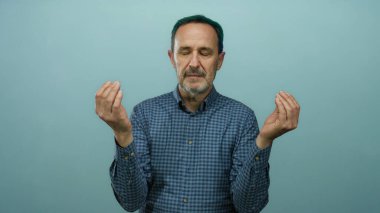 Mavi bir duvarın önünde gözleri kapalı meditasyon yapan, kareli bir gömlek giyen, sakinliği, huzuru ve içgözlem yeteneğini yakalayan, rahatlama ve farkındalık temaları için mükemmel bir adam..