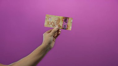 İzole edilmiş mor arkaplan üzerinde Kanada banknotu tutan adam, minimalist bir ortamda para sergiliyor, finansal kavramları vurguluyor ve ulusal kimliği vurguluyor.
