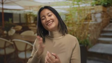 Şehirdeki açık hava restoranının terasında gülümseyen kadın elleri göğsünde, mutluluğu ve sıcaklığı iletiyor..