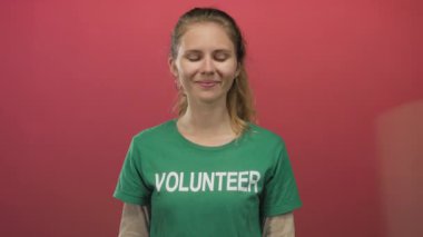 Kadın yeşil gömleğin üzerine gönüllü eldiven ve naylon sarma yaparken sarı saçı ise kapalı bir ortamda hafif bir gülümseme çerçevesi takıyor..