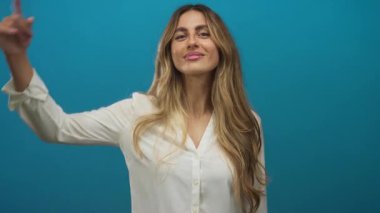 Mavi fotoğraf stüdyosunda beyaz bluzlu, uzun sarı saçlı, yanak yanağa gezen, neşeli, kendine güveni tam bir kadın..