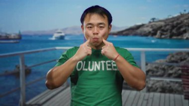 Yeşil tişörtlü bir adam deniz kenarındaki sahil yolunda resimli bir şekilde poz veriyor..