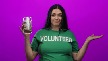 Gönüllü bir kadın, dolarlar dolusu parayı canlı pembe bir arka plana karşı elinde tutuyor, hayır işi yapıyor ve özgüvenli bir ifadeyle bağış toplama çabaları sergiliyor.