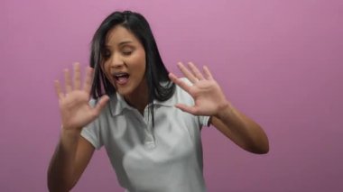 Canlı pembe bir arka plana karşı şaşırmış bir şekilde elini kaldıran bir kadın izole edilmiş bir sahnede duygu ve ifade aktarıyor..