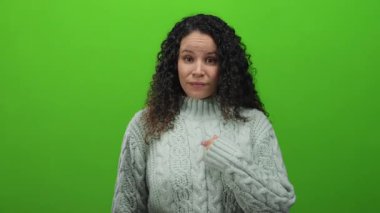 Kablolu örgü süveter giyen İspanyol kadın gülümsüyor ve canlı yeşil arka plana başparmak sallayarak olumlu duygular ve onay veriyor..