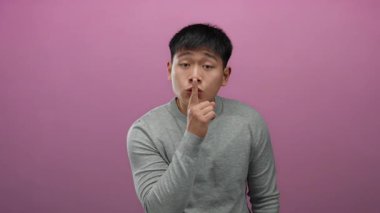 Pembe arka planda dudakları üstünde sessizlik için el kol hareketi yapan genç adam gizemli ve sakin bir ortam izlenimi uyandırıyor..