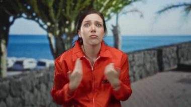 Turuncu hapishane tulumu giymiş bir kadın sahilde geziniyor taş bir duvar ve okyanus manzaralı tedirgin görünüyor. Endişe ve yalnızlık duyguları yakalıyor..