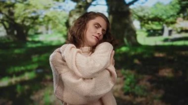 Genç bir kadın, yemyeşil ağaçlarla çevrili sakin bir park ortamında mutlu bir şekilde kendini kucaklıyor. Huzurlu bir yalnızlık ve kendini beğenmişlik anı öneriyor..