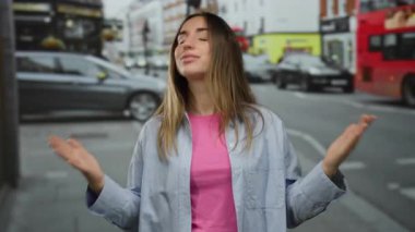 Pembe gömlekli ve mavi ceketli sarışın genç bir kadın kalabalık bir şehir caddesinde arka planda arabalar ve binalarla sürpriz yapıyor..