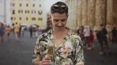 Çiçekli tişörtlü İspanyol genç adam hareketli şehir caddesinde dondurma yiyor, bir turistin açık hava anını yakalıyor.