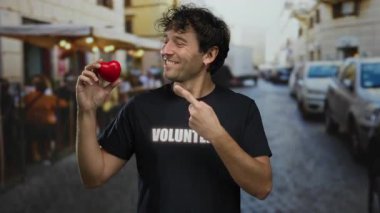 Kırmızı bir kalple sokakta sırıtan İspanyol bir adam. Gönüllü bir tişört giyiyor. Yardım ve toplum ruhunu tasvir ediyor..