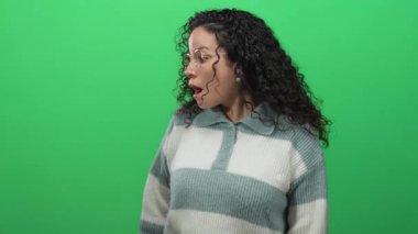 Canlı yeşil arkaplan üzerinde çizgili süveterle duygularını ifade eden bir kadın, izole bir arkaplanda canlı bir atmosferle şaşırtıcı ve merak uyandırıyor..